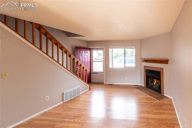 unfurnished living room with a textured ceiling, light hardwood / wood-style flooring, and a tile fireplace