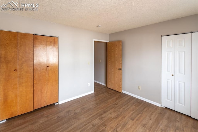 unfurnished bedroom with a textured ceiling, two closets, and dark wood-type flooring