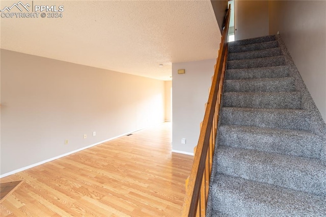 staircase with a textured ceiling and hardwood / wood-style floors