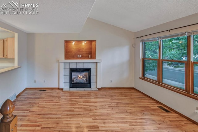 unfurnished living room with lofted ceiling, a tiled fireplace, light hardwood / wood-style floors, and a textured ceiling