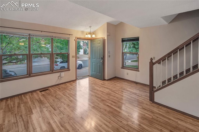 foyer with a wealth of natural light, light hardwood / wood-style flooring, vaulted ceiling, and a notable chandelier