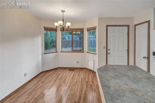 unfurnished dining area with an inviting chandelier, plenty of natural light, light hardwood / wood-style floors, and radiator