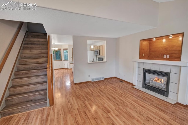 unfurnished living room featuring light wood-type flooring, a chandelier, and a tiled fireplace