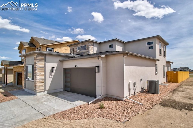 view of front of home with fence, central air condition unit, stucco siding, stone siding, and driveway