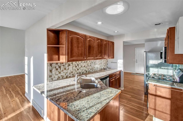 kitchen featuring light stone counters, backsplash, stainless steel appliances, light hardwood / wood-style flooring, and sink