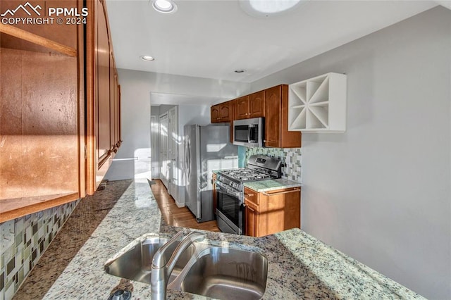 kitchen featuring light stone counters, backsplash, stainless steel appliances, light wood-type flooring, and sink