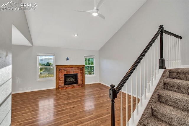 living room featuring high vaulted ceiling, hardwood / wood-style floors, ceiling fan, and a brick fireplace