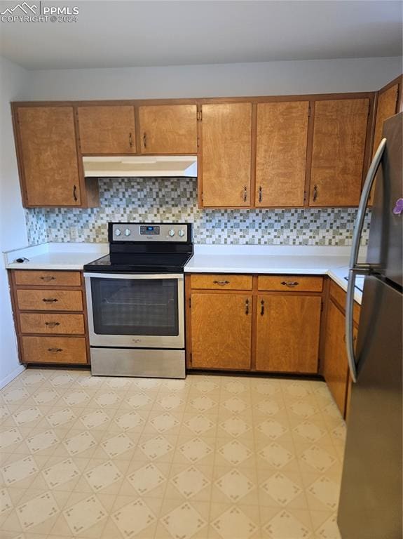 kitchen with stainless steel range with electric stovetop, light floors, under cabinet range hood, and freestanding refrigerator