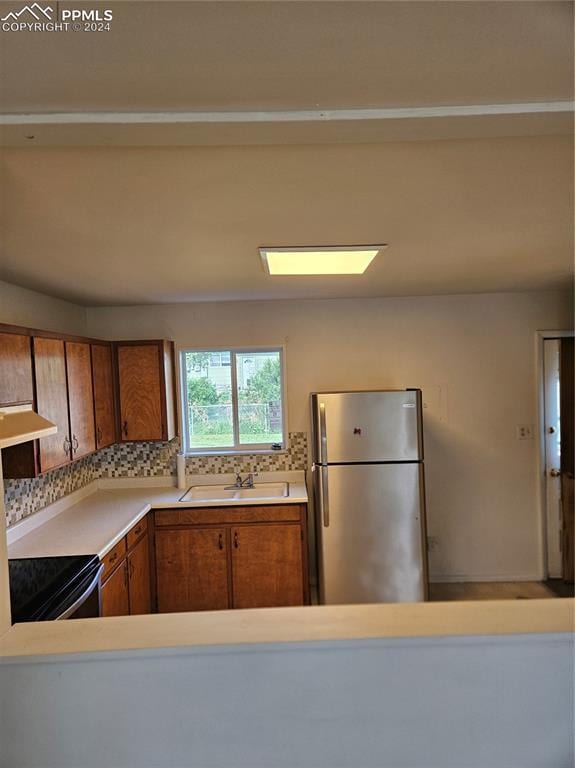 kitchen with light countertops, a sink, range with electric stovetop, freestanding refrigerator, and brown cabinets