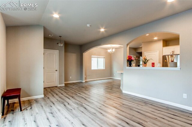 unfurnished living room with light hardwood / wood-style floors, lofted ceiling, and a chandelier