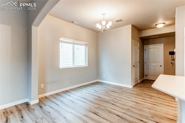 empty room featuring a notable chandelier and light hardwood / wood-style flooring