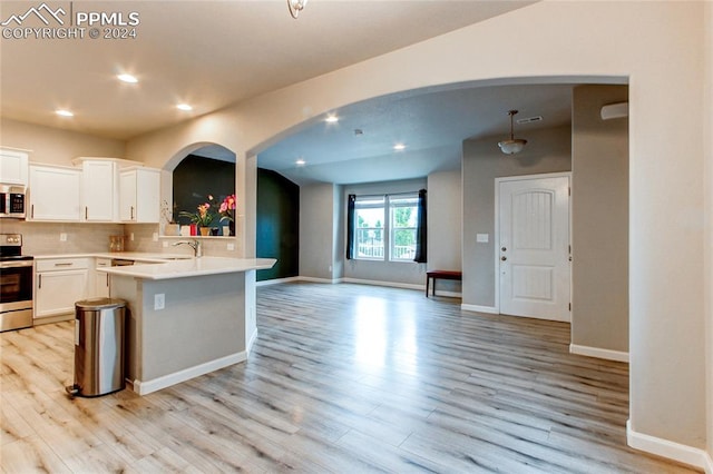 kitchen with appliances with stainless steel finishes, white cabinetry, light wood-type flooring, and hanging light fixtures