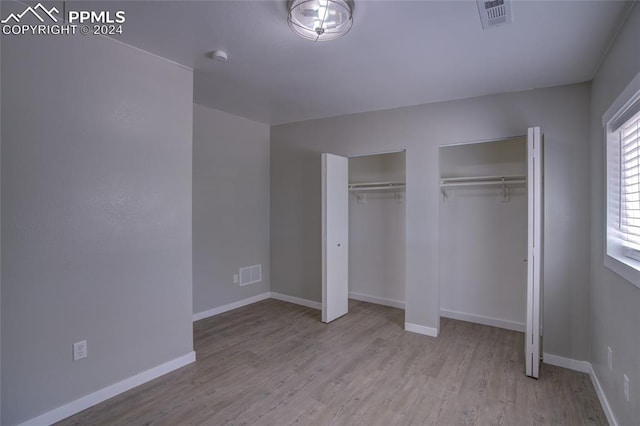 unfurnished bedroom featuring multiple closets and light hardwood / wood-style flooring