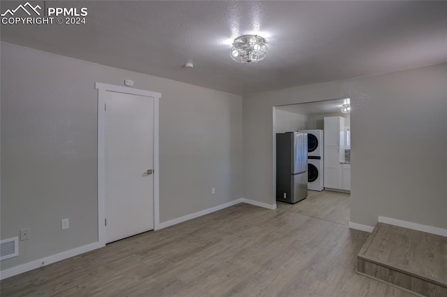 unfurnished room featuring light hardwood / wood-style flooring and stacked washer and clothes dryer