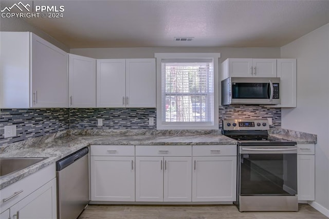 kitchen with white cabinetry, stainless steel appliances, tasteful backsplash, and light wood-type flooring