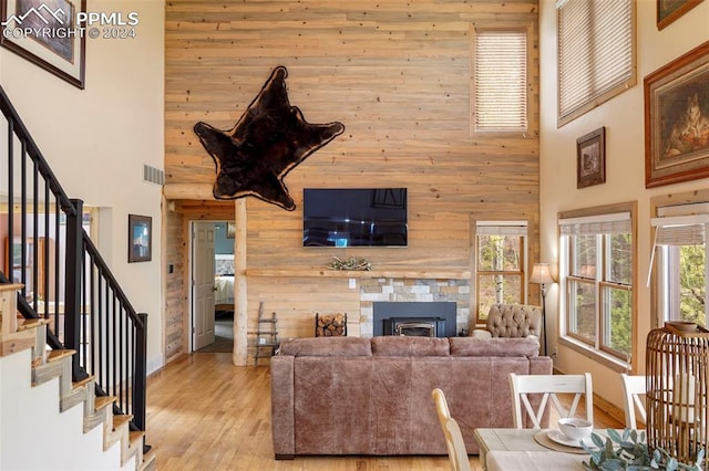 living room with light wood-type flooring, a towering ceiling, plenty of natural light, and wood walls