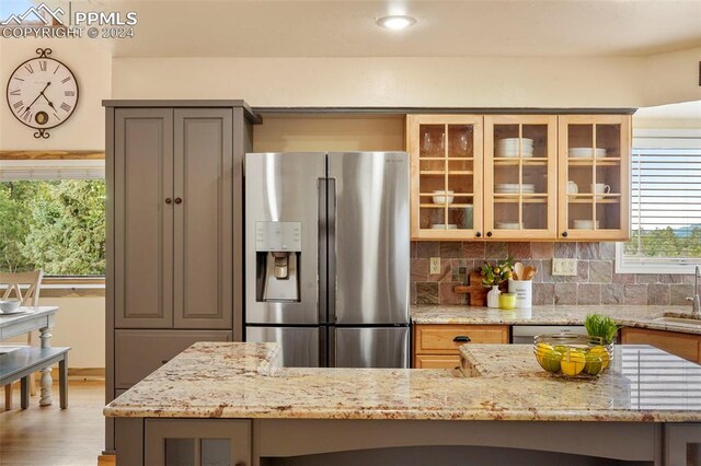 kitchen featuring backsplash, sink, hardwood / wood-style flooring, light stone counters, and stainless steel refrigerator with ice dispenser