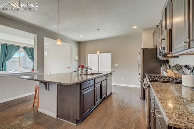 kitchen with stainless steel appliances, a kitchen island with sink, dark hardwood / wood-style flooring, and light stone counters