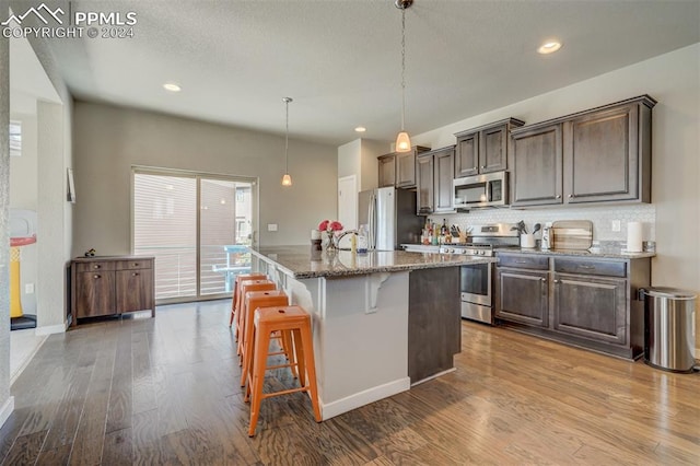 kitchen featuring dark stone counters, a kitchen island with sink, hardwood / wood-style floors, a kitchen bar, and appliances with stainless steel finishes