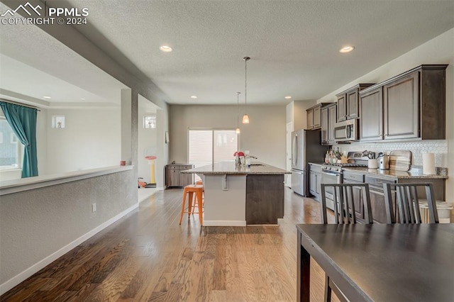 kitchen with stainless steel appliances, light hardwood / wood-style flooring, light stone countertops, a kitchen island with sink, and a breakfast bar