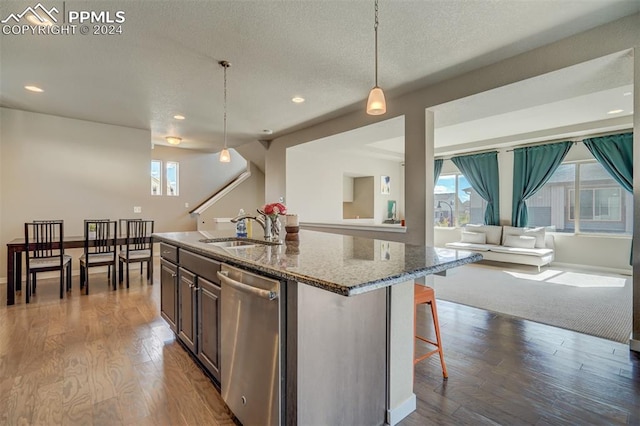 kitchen with light hardwood / wood-style flooring, dishwasher, sink, stone countertops, and pendant lighting