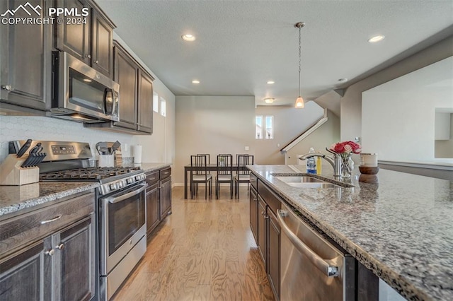 kitchen featuring light hardwood / wood-style flooring, dark brown cabinetry, sink, dark stone countertops, and stainless steel appliances