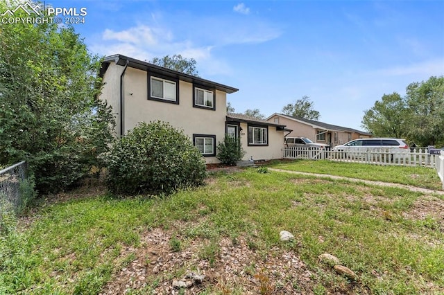 rear view of house with a yard, fence, and stucco siding