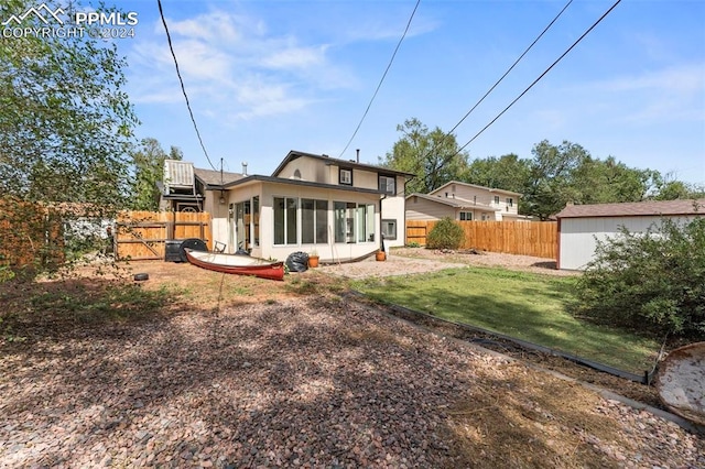 back of house featuring a sunroom, a fenced backyard, a storage unit, and an outbuilding