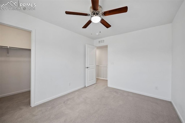 unfurnished bedroom featuring ceiling fan, a walk in closet, and light carpet