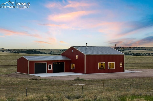 back house at dusk featuring a garage, a rural view, and an outbuilding