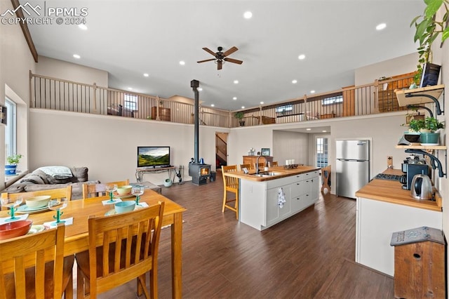 kitchen with ceiling fan, a wood stove, white cabinets, sink, and stainless steel fridge