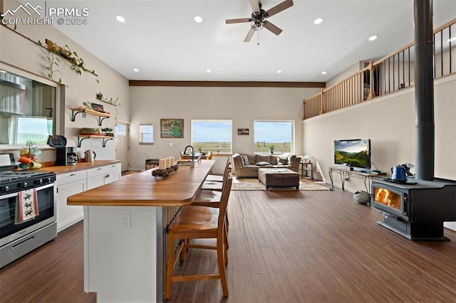 kitchen featuring butcher block counters, a wood stove, white cabinets, stainless steel range with gas stovetop, and dark wood-type flooring