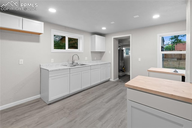 kitchen featuring light wood-type flooring, sink, light stone countertops, and white cabinets