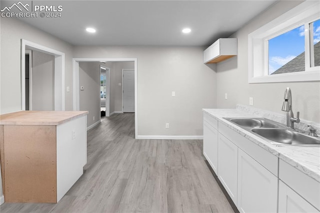 kitchen with light wood-type flooring, sink, wood counters, and white cabinets