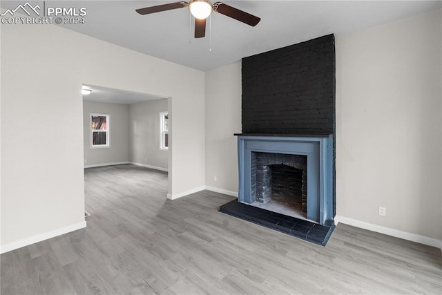 unfurnished living room featuring ceiling fan, a fireplace, hardwood / wood-style floors, and brick wall