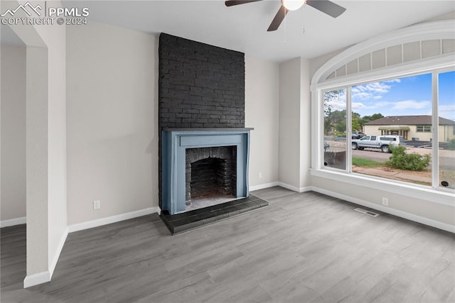 unfurnished living room with hardwood / wood-style floors, a large fireplace, brick wall, and ceiling fan