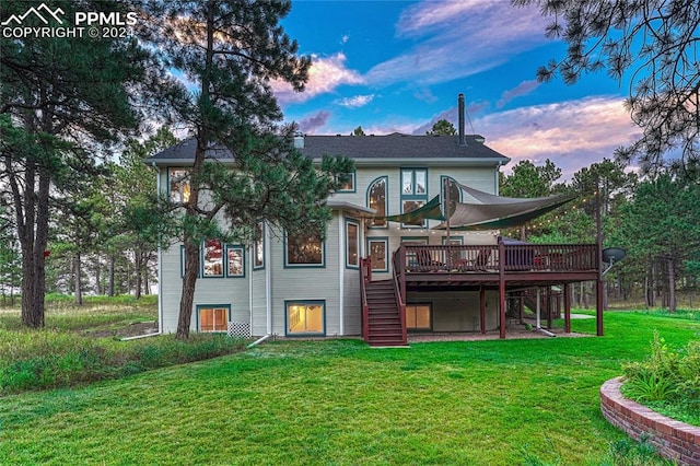 back house at dusk featuring a lawn and a deck