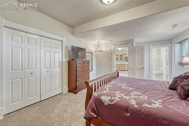 carpeted bedroom featuring a textured ceiling, connected bathroom, a notable chandelier, and a closet