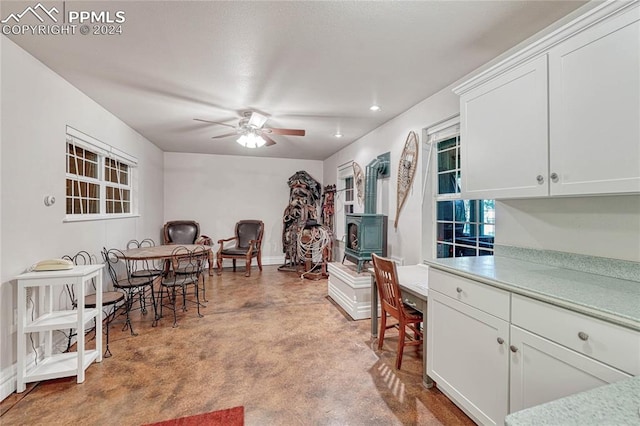 kitchen with ceiling fan, a wood stove, and white cabinetry