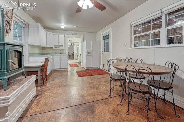 kitchen with concrete floors, white fridge with ice dispenser, white cabinetry, sink, and ceiling fan