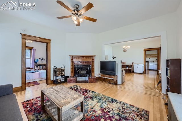 living room with a fireplace, ceiling fan with notable chandelier, and light hardwood / wood-style floors