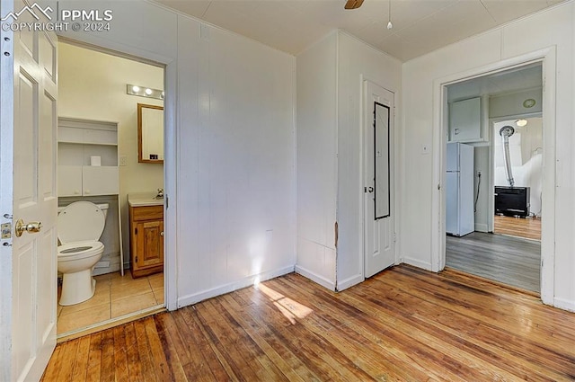 unfurnished bedroom with ensuite bathroom, light wood-type flooring, and freestanding refrigerator