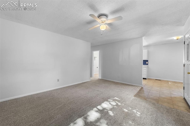 empty room with ceiling fan, light colored carpet, and a textured ceiling