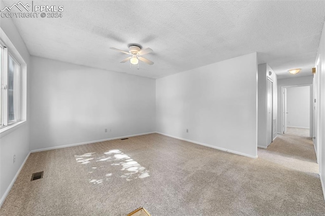 spare room featuring ceiling fan, light colored carpet, and a textured ceiling