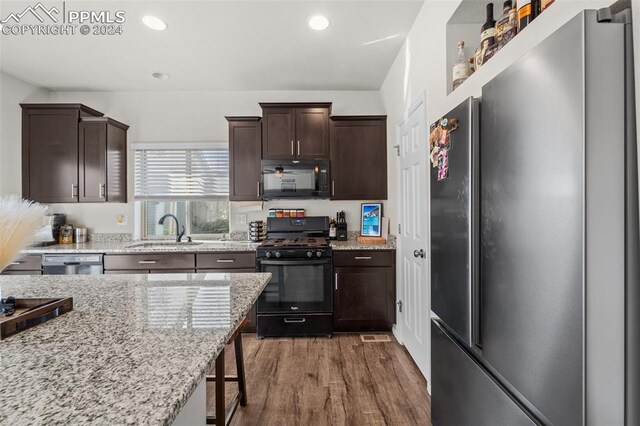 kitchen with sink, wood-type flooring, dark brown cabinets, light stone countertops, and black appliances