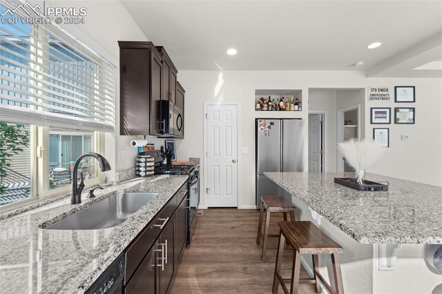 kitchen with sink, dark hardwood / wood-style flooring, dark brown cabinets, light stone counters, and stainless steel appliances