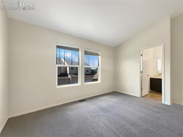 unfurnished bedroom featuring carpet floors, lofted ceiling, and connected bathroom