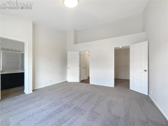 unfurnished bedroom with carpet floors, a high ceiling, a walk in closet, and ensuite bath