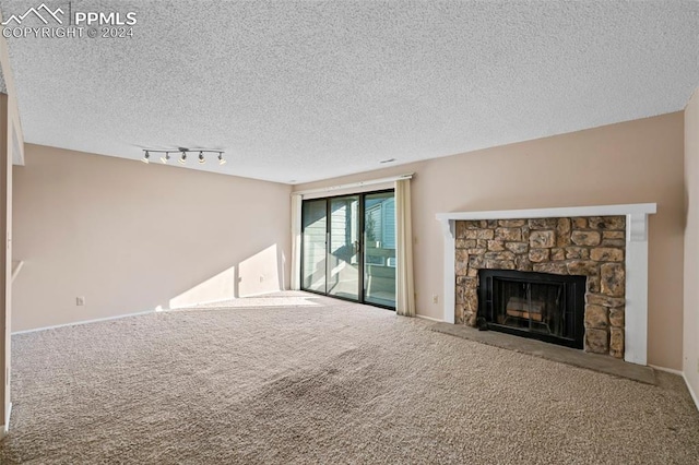 unfurnished living room with a textured ceiling, rail lighting, carpet, and a stone fireplace