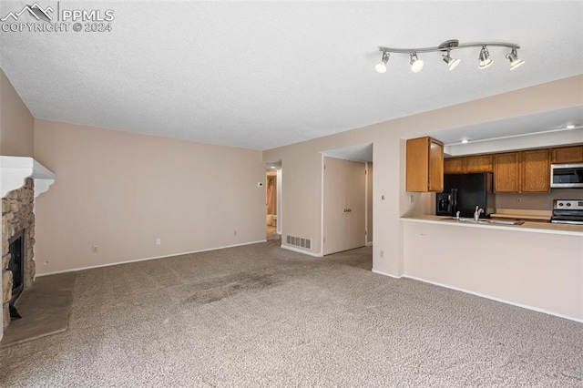 unfurnished living room with a fireplace, track lighting, sink, and light colored carpet